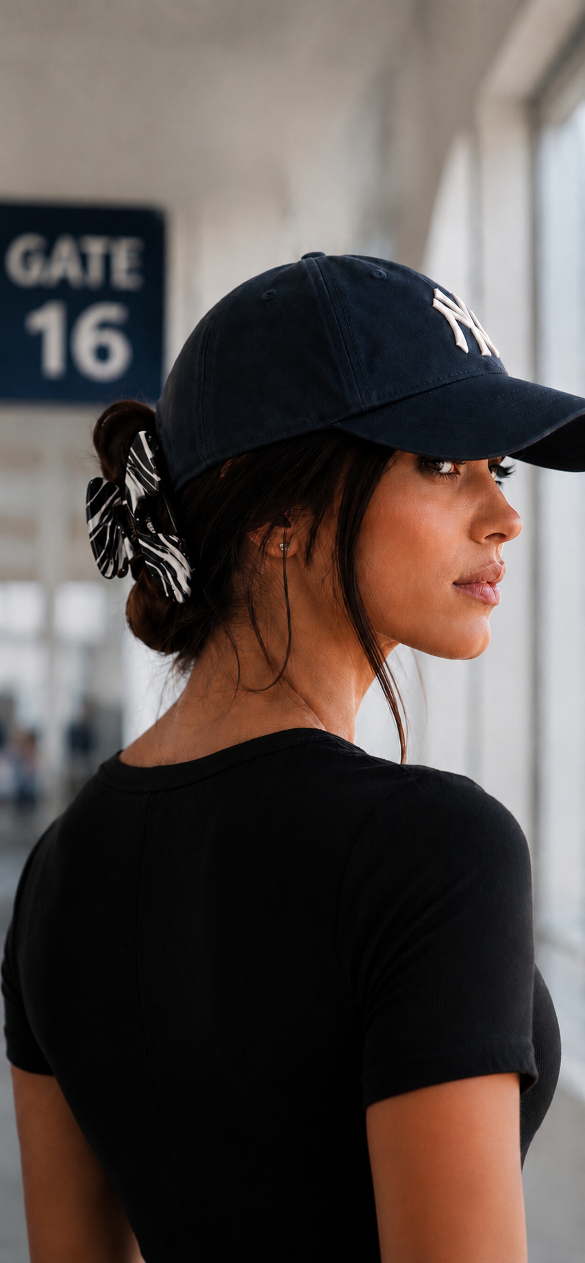 Woman in a navy baseball cap at an airport gate with her hair clipped up in a Baddie Clip hat claw clip. 