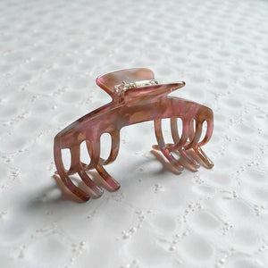 Blush pink hat claw clip displayed on a soft textured surface for an everyday lifestyle product view.