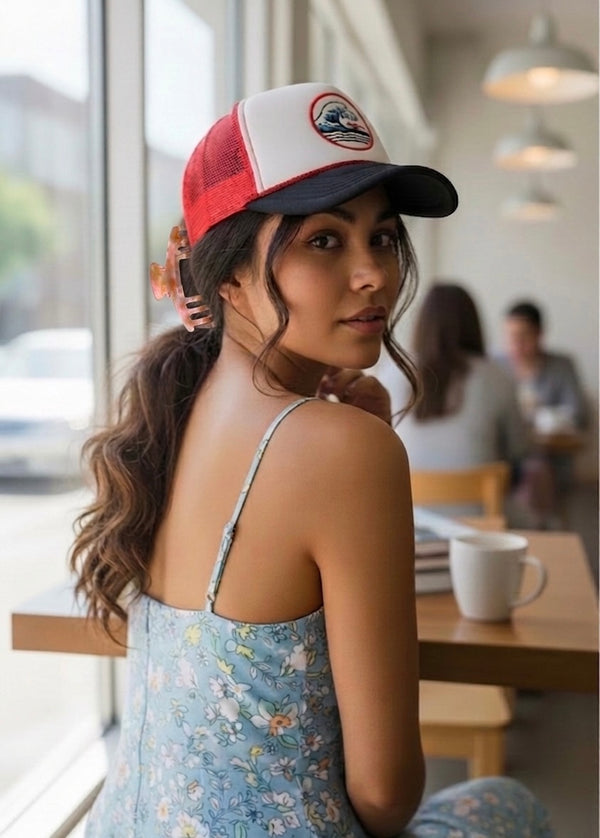 Woman in a coffee shop wearing a red and white trucker hat with her hair clipped up in a Blush pink Baddie Clip hat claw clip.