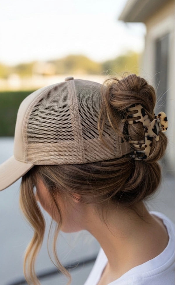 Woman wearing a beige trucker hat, hair pulled into a messy bun with an Essential Hold claw clip in Hazel, outdoors