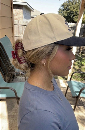 Woman wearing a beige and navy cap, hair pulled into a bun with an Essential Hold claw clip in Merlot, sitting outdoors