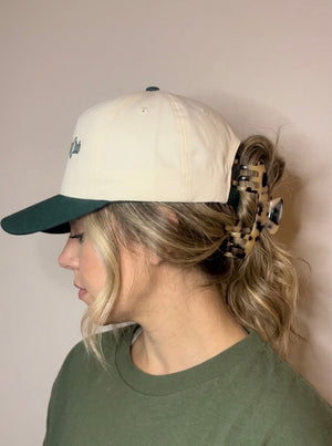Side view of a woman wearing a cream and green baseball cap with her hair clipped up in a Hazel tortoiseshell Baddie Clip hat claw clip.