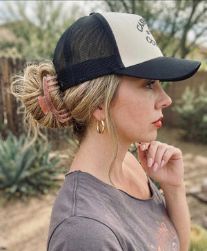 Woman wearing a black and beige trucker hat, hair pulled into a bun with an Essential Hold claw clip in Blush, in a desert setting
