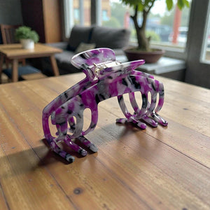 Orchid purple marble hat claw clip displayed on a wooden table in a casual indoor setting.