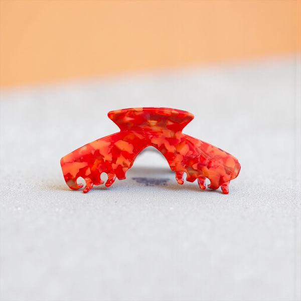 Scarlet red mosaic hat claw clip displayed on a tabletop, highlighting its bright finish and everyday style.