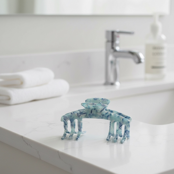 Sea Glass blue marble claw clip displayed on a bathroom counter in a bright neutral setting.