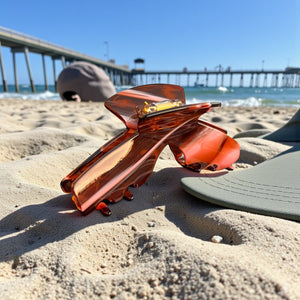 Siren amber tortoise hat claw clip on a sandy beach with a baseball hat, ideal for travel, vacations, and all-day secure hairstyles.