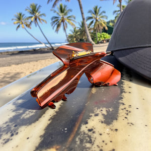 Siren amber tortoise hat claw clip displayed beside a baseball hat, designed to work comfortably with hats and securely hold medium to thick hair.
