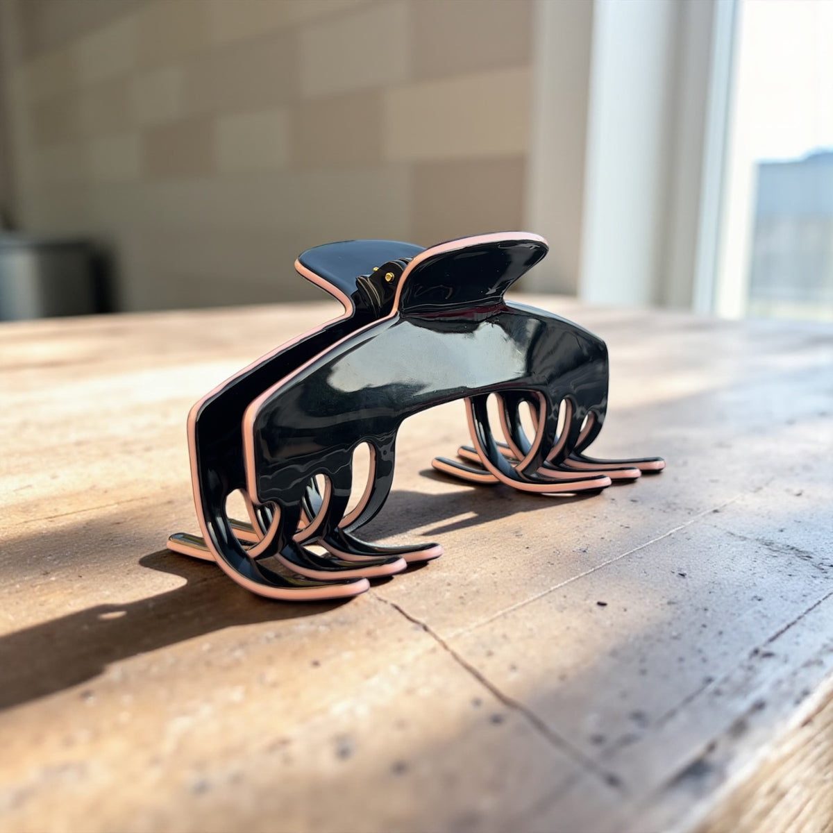 Onyx Black and rose gold hat claw clip on a wooden surface, designed to hold hair securely under baseball caps and trucker hats.